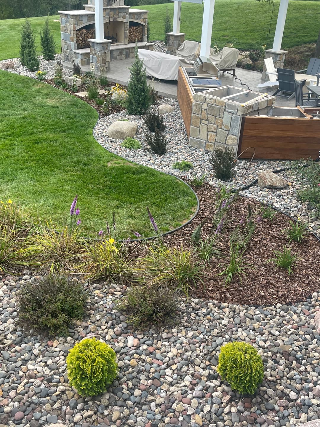 Lush landscaped yard featuring stone patio, fire pit, and vibrant flower beds.