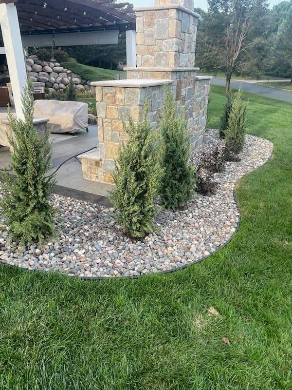 Landscaped yard featuring a stone wall, shrubs, and decorative gravel border.