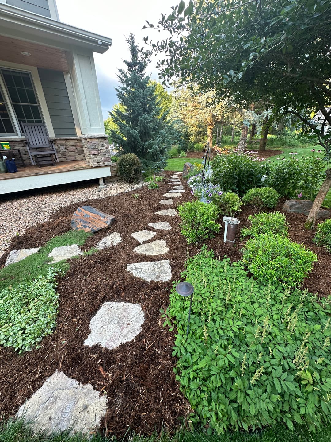 Stone path winding through a landscaped garden with shrubs, plants, and decorative lighting.