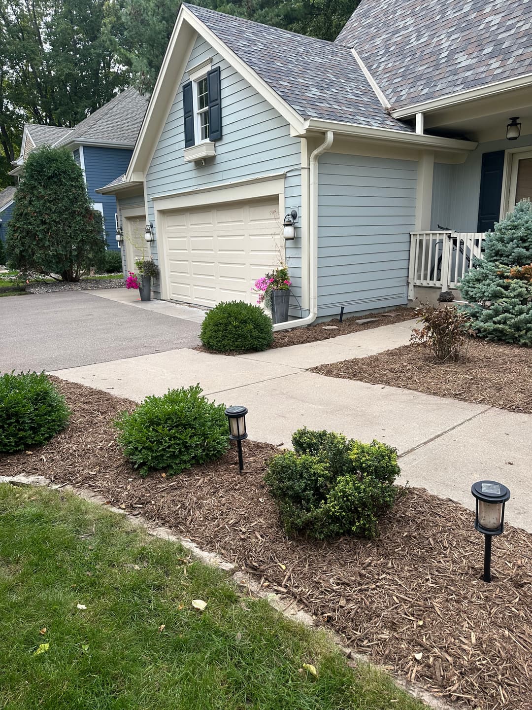 Blue house with a light garage door, landscaped yard, and garden lights along the pathway.