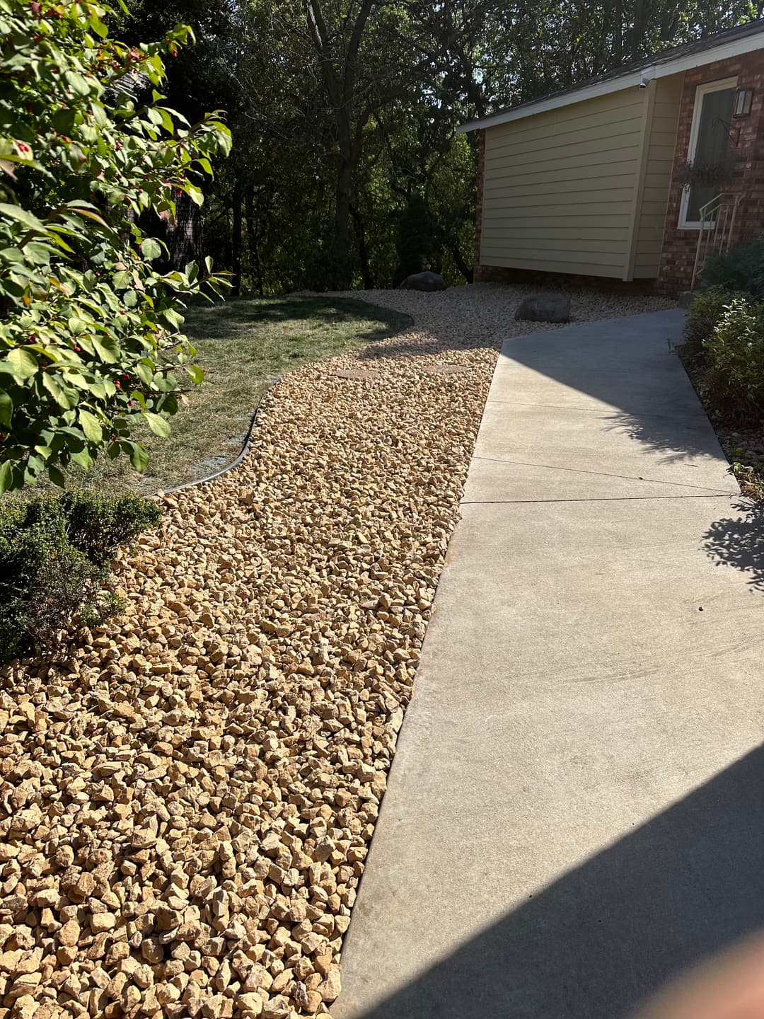 Gravel landscaping along a concrete path leading to a house in a green garden setting.