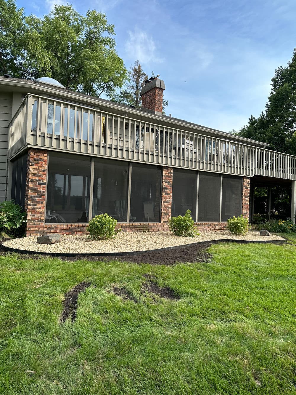 Screened porch with brick exterior, landscaped lawn, and clear sky in background.